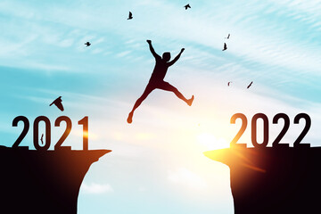 Silhouette man jumping between cliff with number 2021 to 2022 and birds flying at top of mountain....