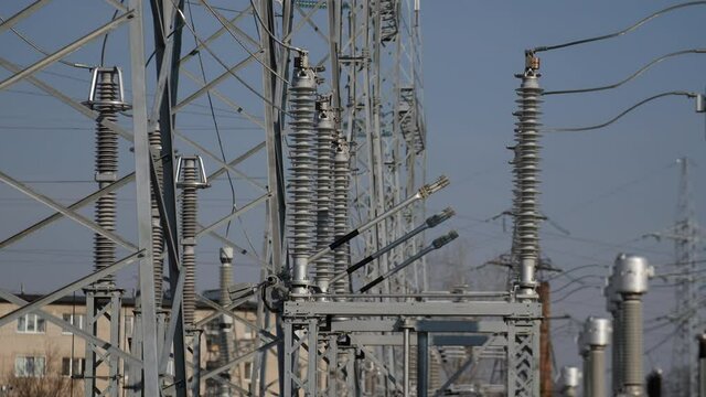 Metal bars go down to platform operating near glass insulators on electricity production substation switchyard on sunny day