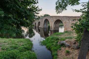 Fototapeta na wymiar The so-called Old Bridge or Romanesque Bridge crosses the Alberche River as it passes through the Spanish municipality of Navaluenga, in the province of Ávila (Spain)