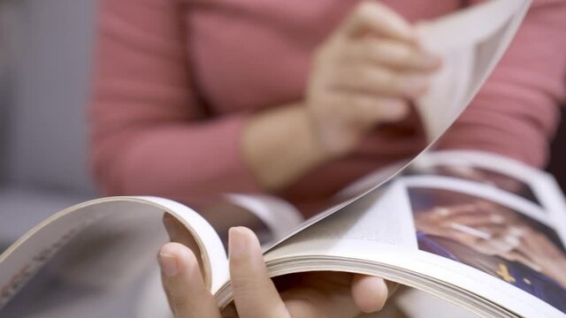 Detail of woman leafing through magazine sitting on sofa.