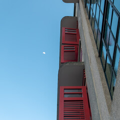 red wooden windows on a building against a blue sky with half moon
