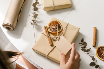 Female hands packing gift decor with dry orange, cinnamon sticks, eucalyptus. Zero waste Christmas