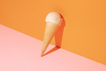 Creative compostition made with ice cream vanilla scoop and cone against pastel pink and orange...