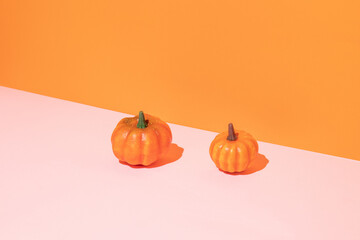Two Halloween pumpkins against pastel pink and orange background. Minimal Holiday season concept background.