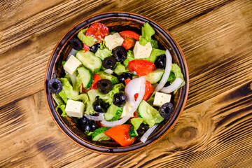 Ceramic plate with greek salad on wooden table. Top view