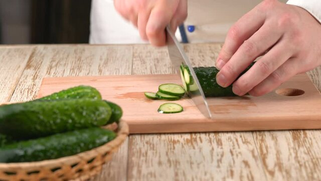 Сhief-cook chopping  fresh cucumber on a wooden cutting board, close up. Chef's hands with knife cutting fresh cucumber.