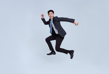 Fototapeta na wymiar Fun portrait of happy energetic young Asian businessman jumping in mid-air isolated on studio white background..