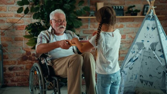 Little girl brings a tray of medicines to an old man in a wheelchair