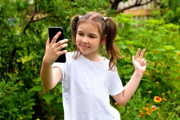 Fototapeta premium A girl with ponytails smiles and communicates via video communication using a smartphone. communication using gadgets.