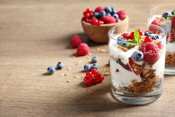 Tasty dessert with yogurt, berries and granola on wooden table. Space for text