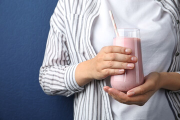 Woman with glass of tasty smoothie on blue background, closeup