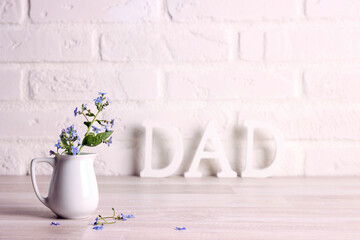Father's day message with forget-me-not flowers in a small jug on the background of a white brick wall.