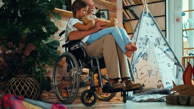 Disabled old man in a wheelchair holds his little granddaughter in his lap