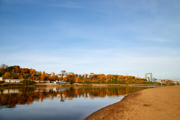 Natural view of the landscape with a lake or river and a city on the other side on the yellow shore in autumn day with blue sky