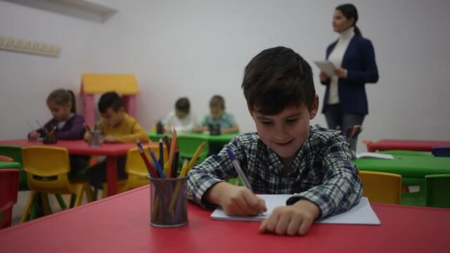 Portrait of little assiduous boy with pen and notebook at lesson in elementary school