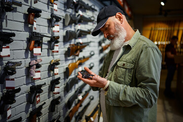 Bearded man holds pistol at showcase in gun store