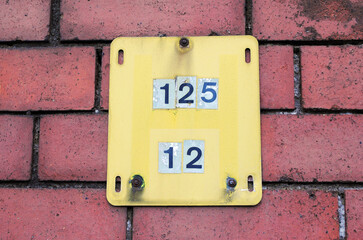 Close Up of Old Yellow Metal Sign with Numbers on Red Brick Wall