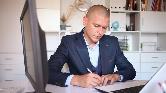 Positive young businessman working with laptop and documents in office. High quality FullHD footage