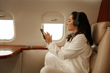 Beautiful girl, a passenger of the plane, having fun during the flight, listening to music and...