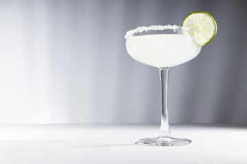 Summer fresh muddy margarita cocktail with sugar rim and slice lime in elegant abstract minimal white and grey interior with striped shadows.