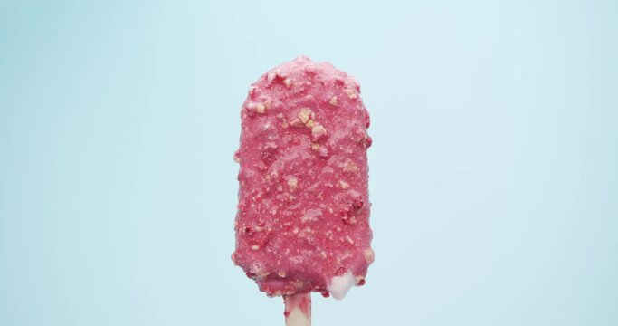 strawberry flavored ice cream popsicle stick coated with creamy almonds on blue background.