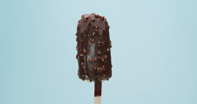 Chocolate flavored ice cream popsicle stick coated with creamy almonds on blue background.