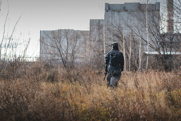 A post apocalypse soldier with a rifle walks through the dried field.
