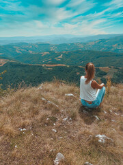 Woman contemplating a beautiful landscape. Happy Woman Enjoying Nature on meadow on top of mountain. Outdoor. Freedom concept. Rear view of a young woman sitting on a mountain top