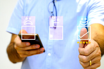 A businessman holding smartphone and pressing smile face emoticon on virtual touch screen. Customer satisfaction survey and questionnaire concept.