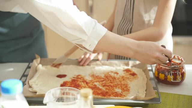 cropped female hand adding sause on pizza base, spreading tomato sauce, preparing for baking, preparing tasty pizza together. At home, in kitchen. domestic atmosphere