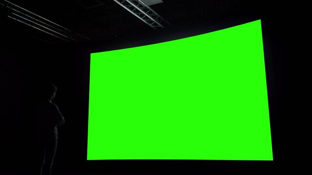 Green screen, technology, chroma key, futuristic, template, mock up, entertainment concept. Woman looking at large wall blank interactive green display in dark room of science exhibition or museum