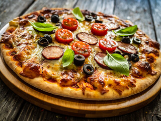 Pizza with white mushrooms, sausage, tomatoes, black olives, parmesan and mozzarella on wooden background
