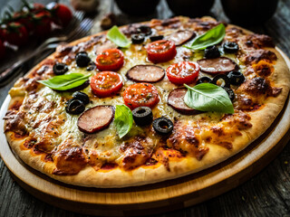 Pizza with white mushrooms, sausage, tomatoes, black olives, parmesan and mozzarella on wooden background
