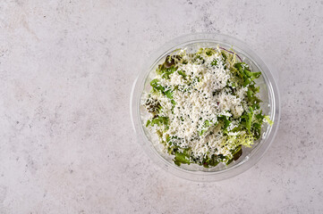 Salad of fresh vegetables with cheese in transparent plastic container. Designer food concept for take away or delivery. Top view, copy space