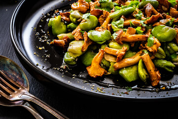 Broad beans salad with fried chanterelles, garlic and parsley on wooden table
