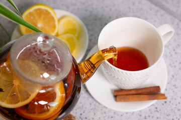 A hot tea drink with lemon and orange, a teapot and a white cup, served with delicious lemon and cinnamon. Fragrant and warming tea. Step 2