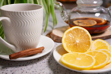 Obraz na płótnie Canvas A hot tea drink with lemon and orange, a teapot and a white cup, served with delicious lemon and cinnamon. Fragrant and warming tea. Step 5