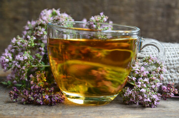 Oregano tea in a glass cup with fresh blooming herb twigs on a wooden background.Healthy drink,diet,alternative therapy or herbal medicine concept.