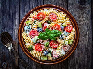 Pasta with fresh vegetables and black olives on wooden table
