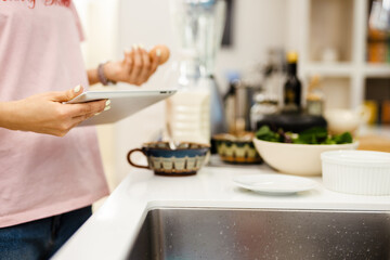 Obraz na płótnie Canvas Black woman using tablet computer while cooking in kitchen at home