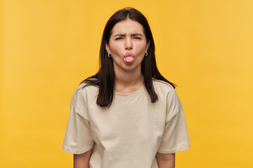 Nasty playful brunette young woman in white tshirt looks naughty and showing tongue over yellow...