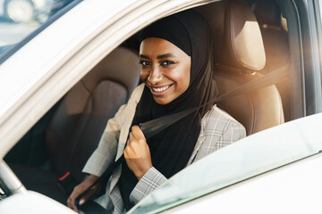 Black muslim woman fastening seat belt while sitting in car