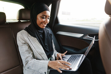 Black muslim woman working with laptop while going in car