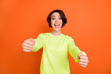Photo of amazed happy cheerful woman hold hands steering wheel smile isolated on orange color background