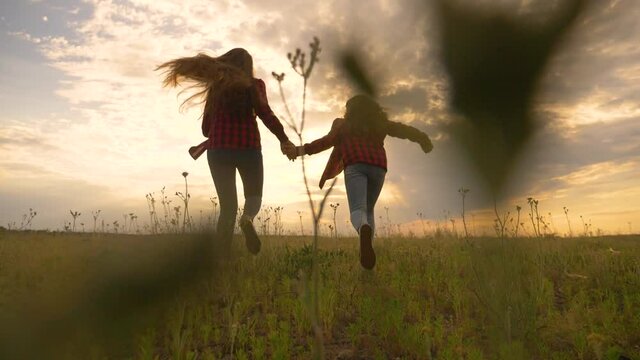 Two happy teenage girls run at sunset together. Girls run hand in hand in the park. Silhouette of children running at sunset in the park.