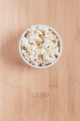 Bowl with popcorn on wooden table.