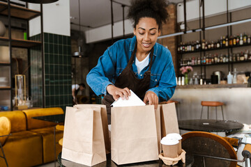 Black waitress in apron packing orders while working at cafe