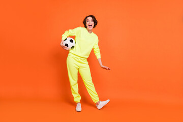Fototapeta na wymiar Full length body size view of attractive cheerful girl holding ball having fun isolated over bright orange color background
