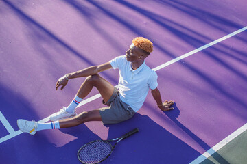 Young man seen sitting on purple colored tennis court