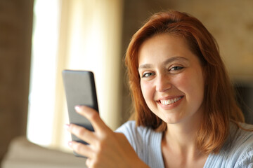 Happy woman holding phone looks at camera at home
